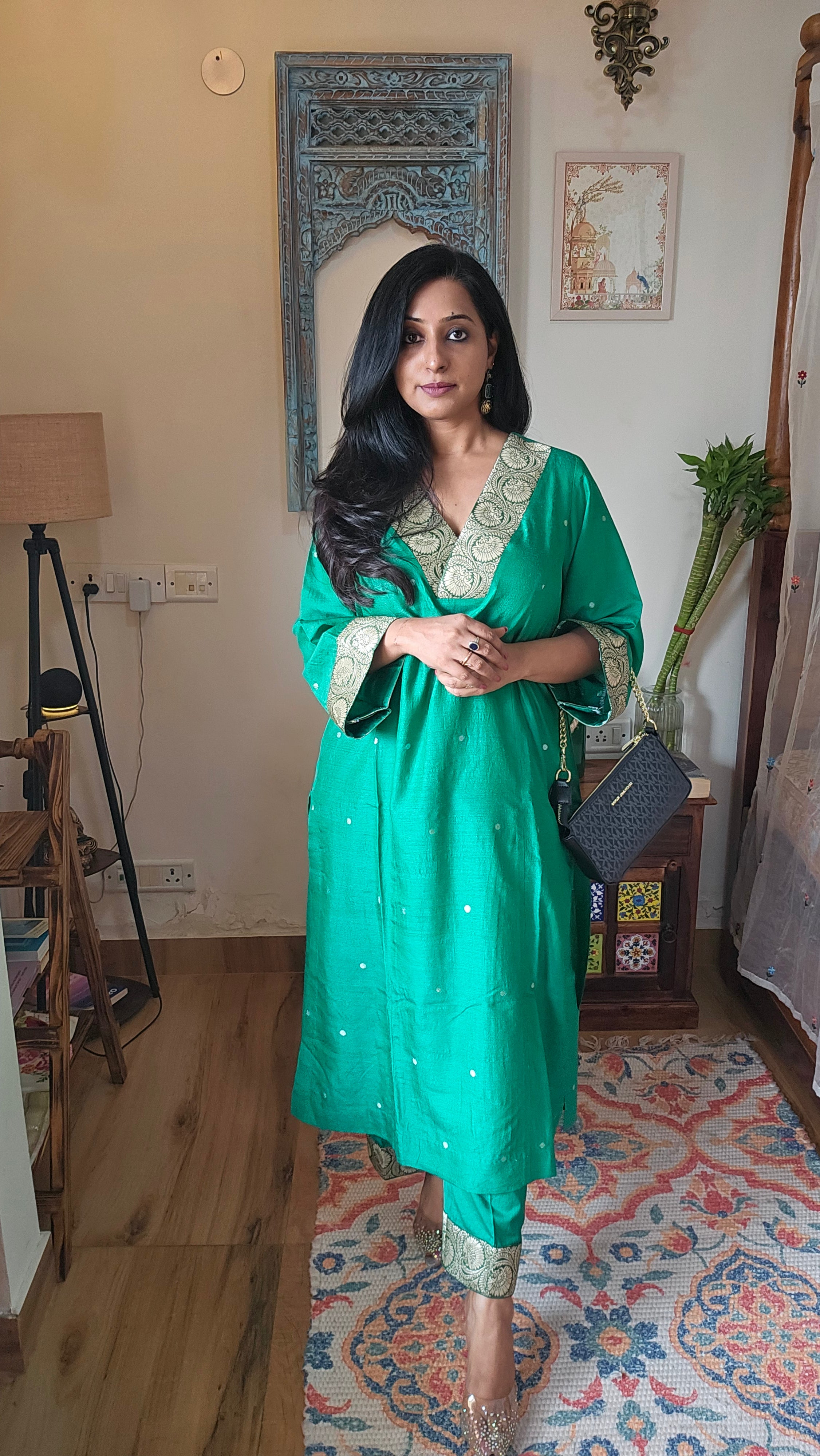 Woman in a green traditional outfit standing in a room with decor elements.