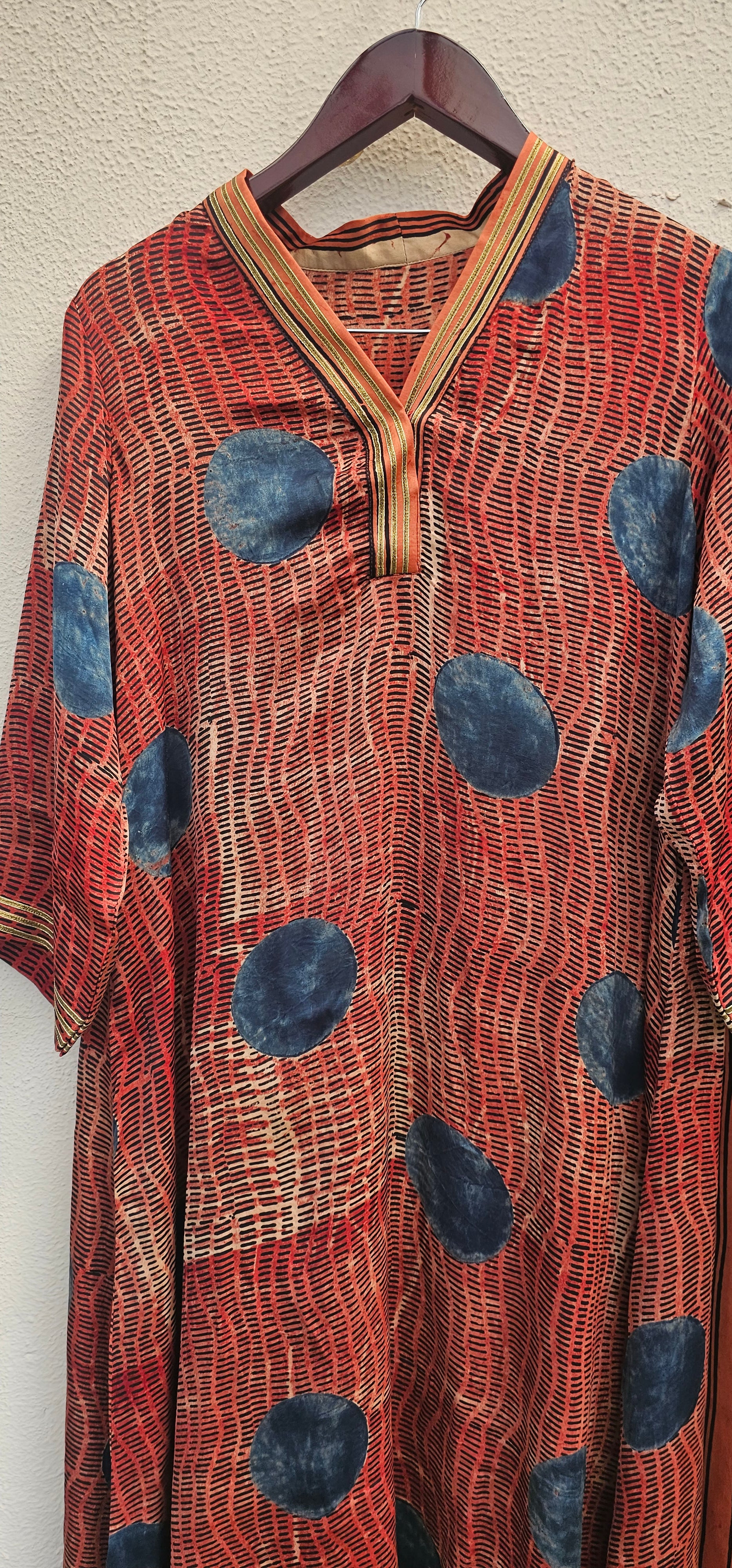 Red patterned dress with blue circles on a hanger against a neutral background