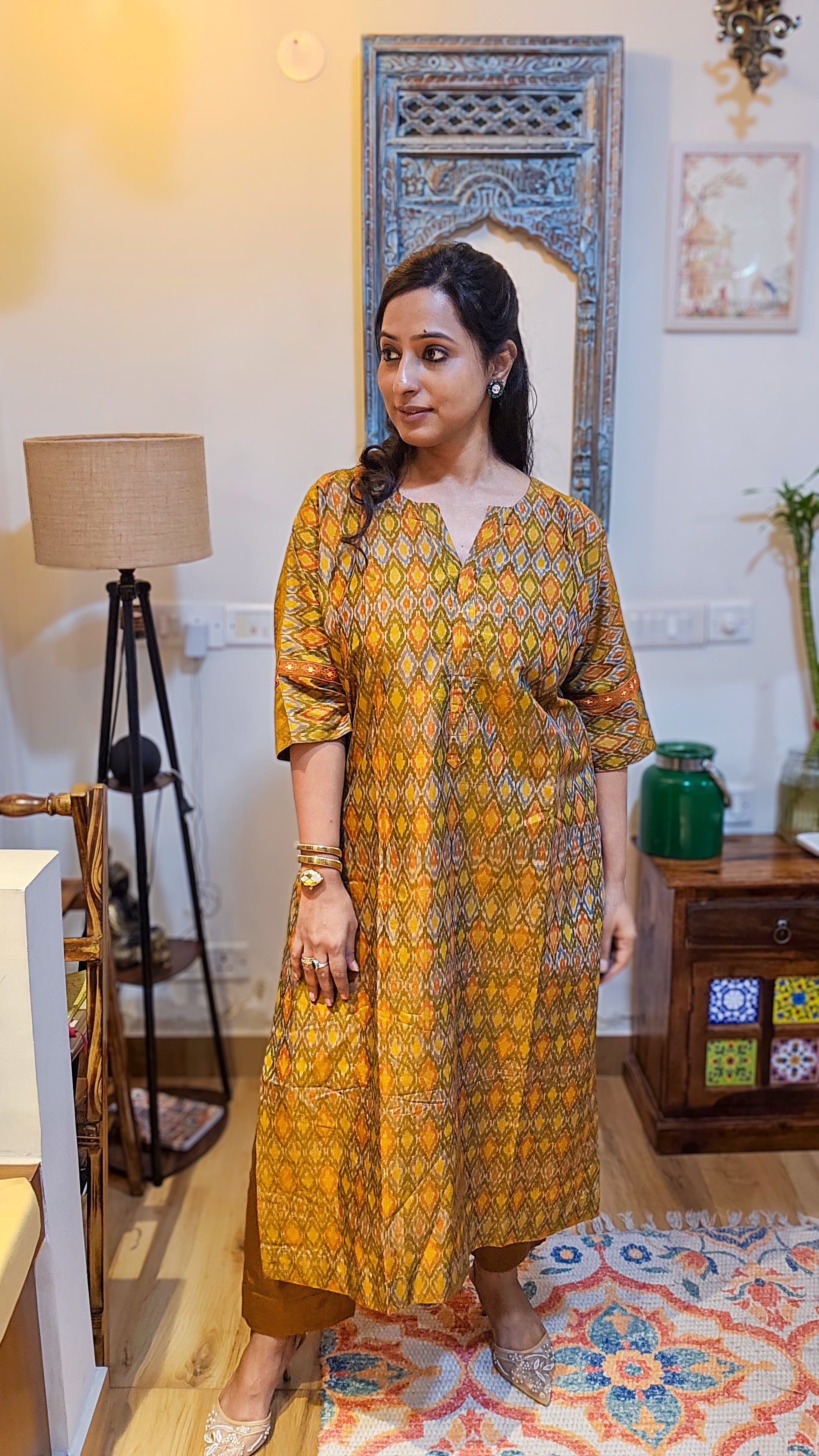 Woman in a yellow patterned dress standing in a room with decorative elements.