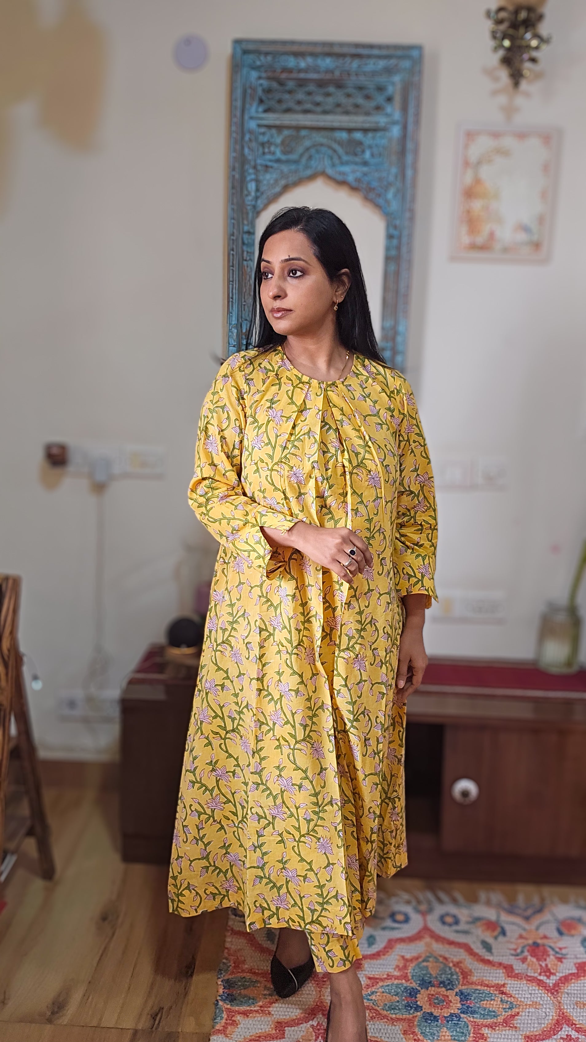 Woman in a yellow floral dress standing in a room with decorative elements.