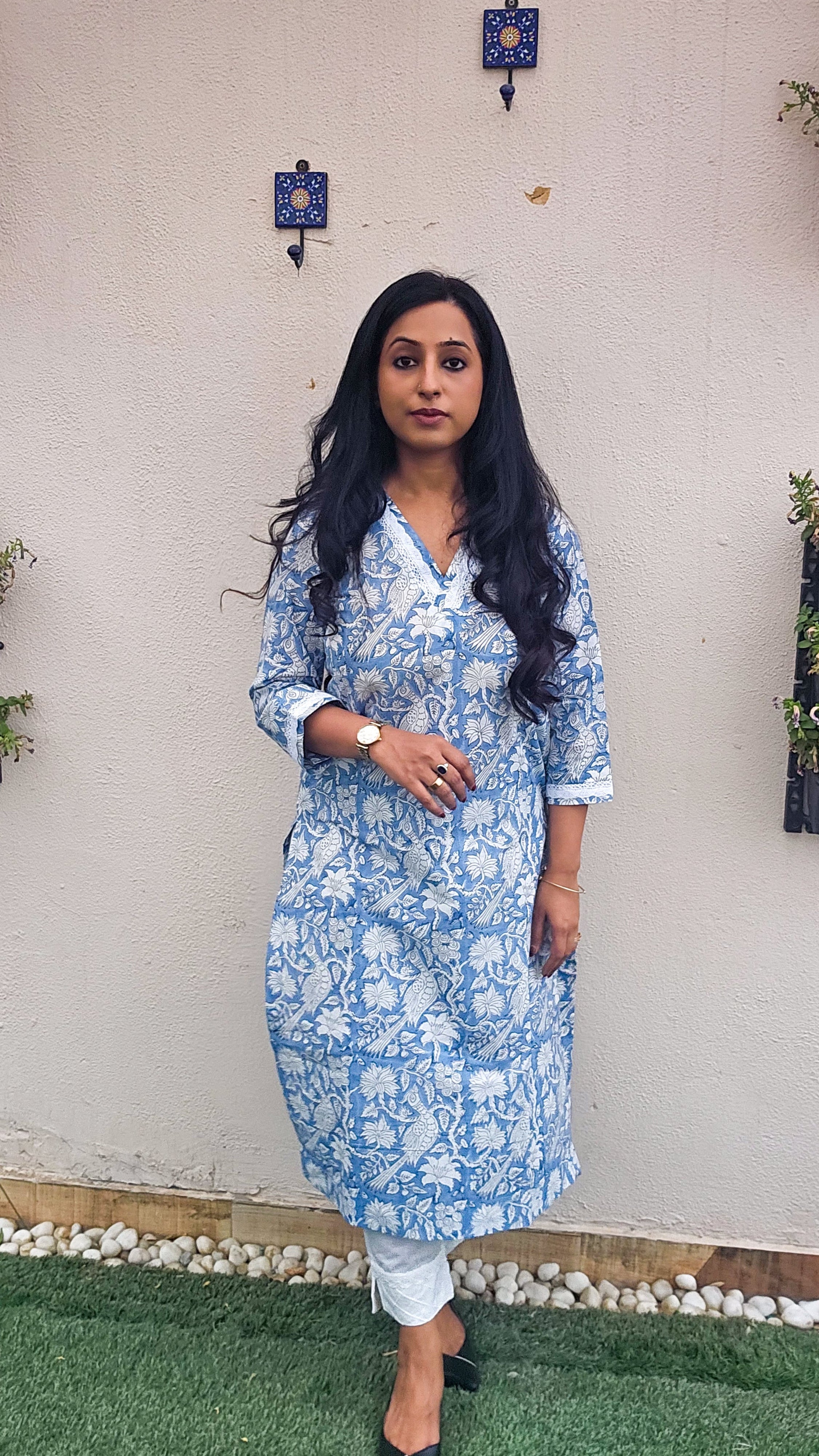 Woman wearing a blue floral with bird motifs hand block print kurta with white pants. Its a pure cotton kurta.
