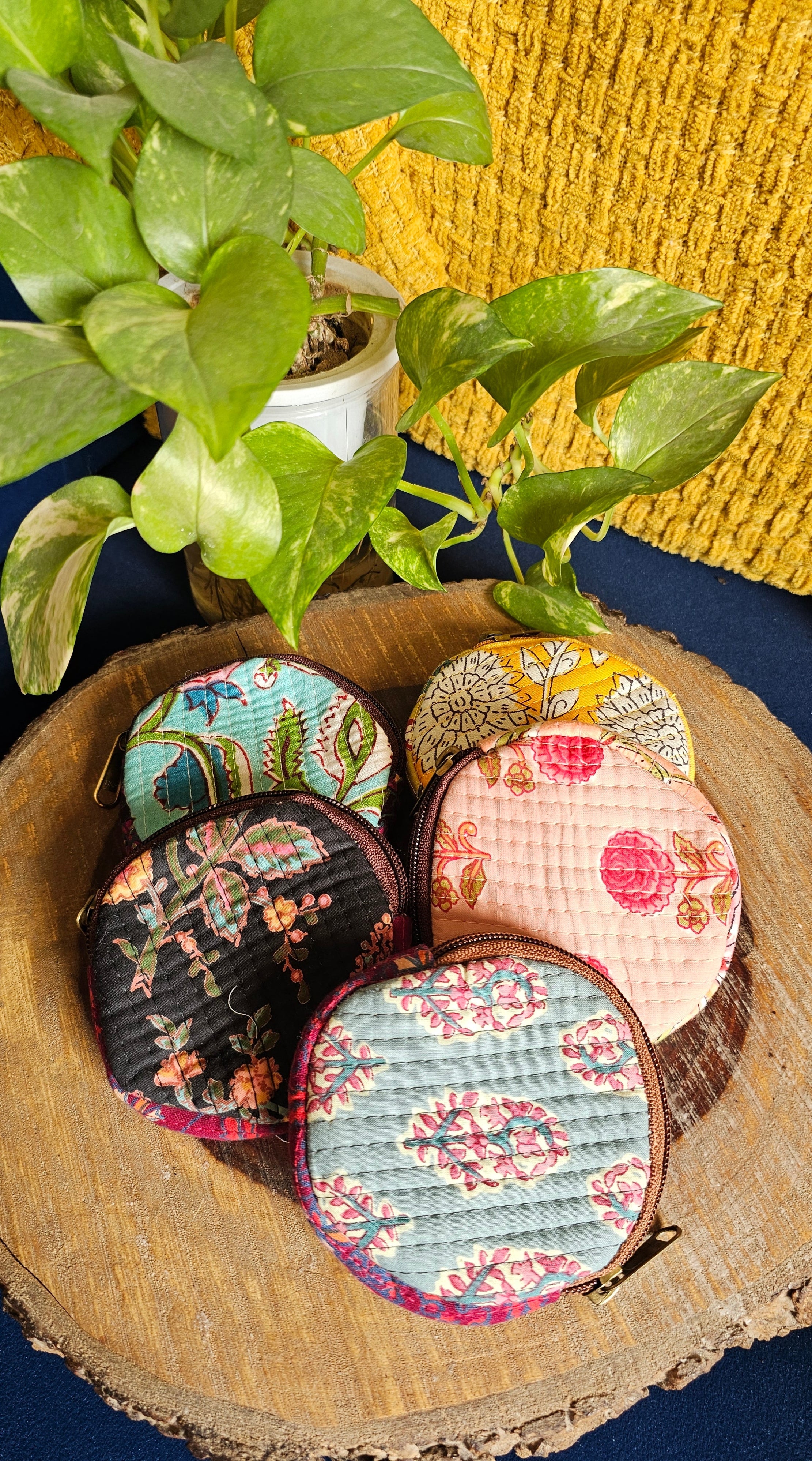 Colorful quilted coin purses on a wooden surface with a plant in the foreground