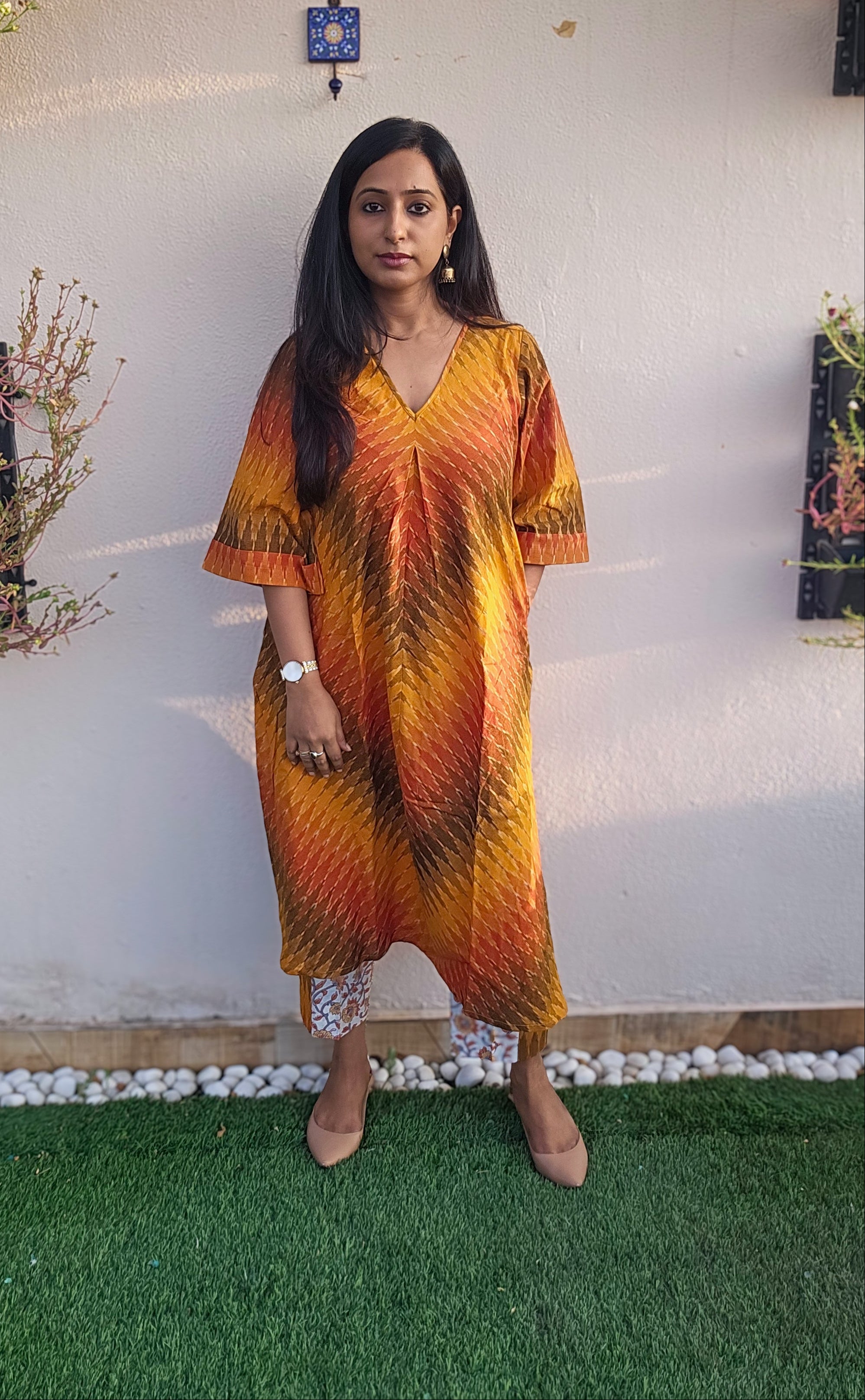 Woman wearing a colorful dress standing in front of a white wall with decorative elements.