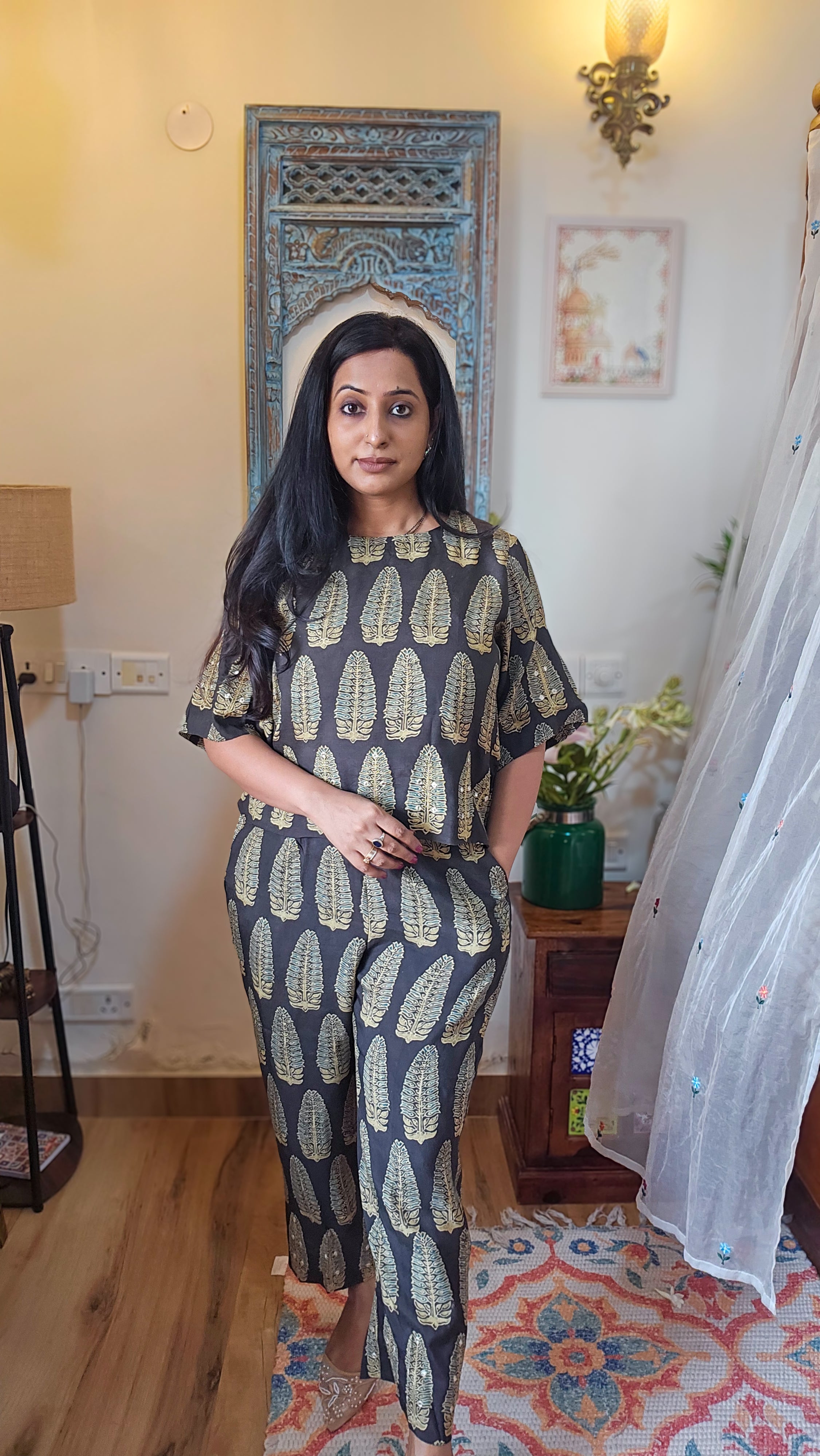 Woman wearing a patterned outfit standing in a room with decorative elements.