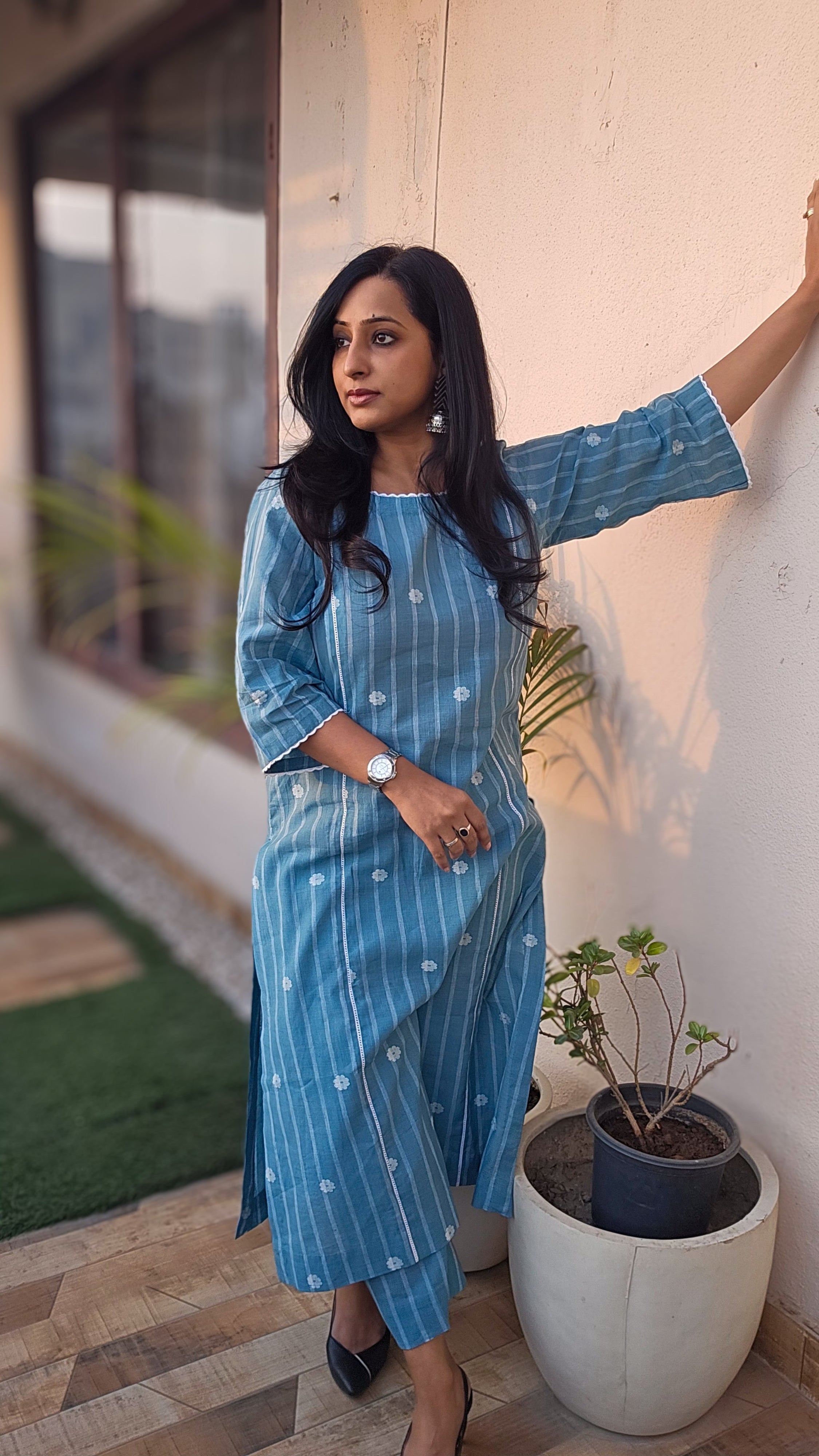 Woman in a blue dress standing by a wall with a plant in the background