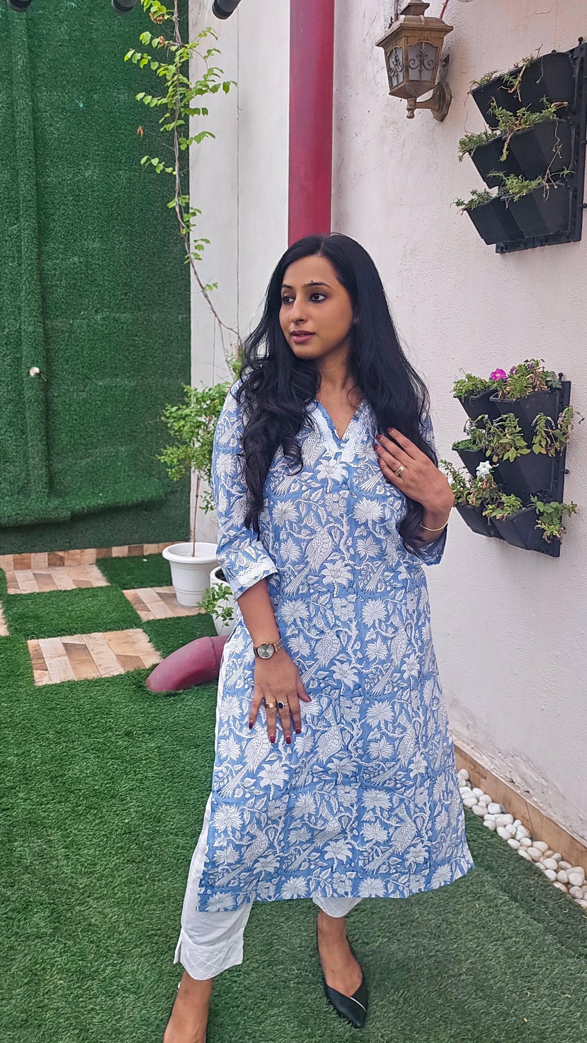 Woman wearing a blue floral with bird motifs hand block print kurta with white pants. Its a pure cotton kurta.