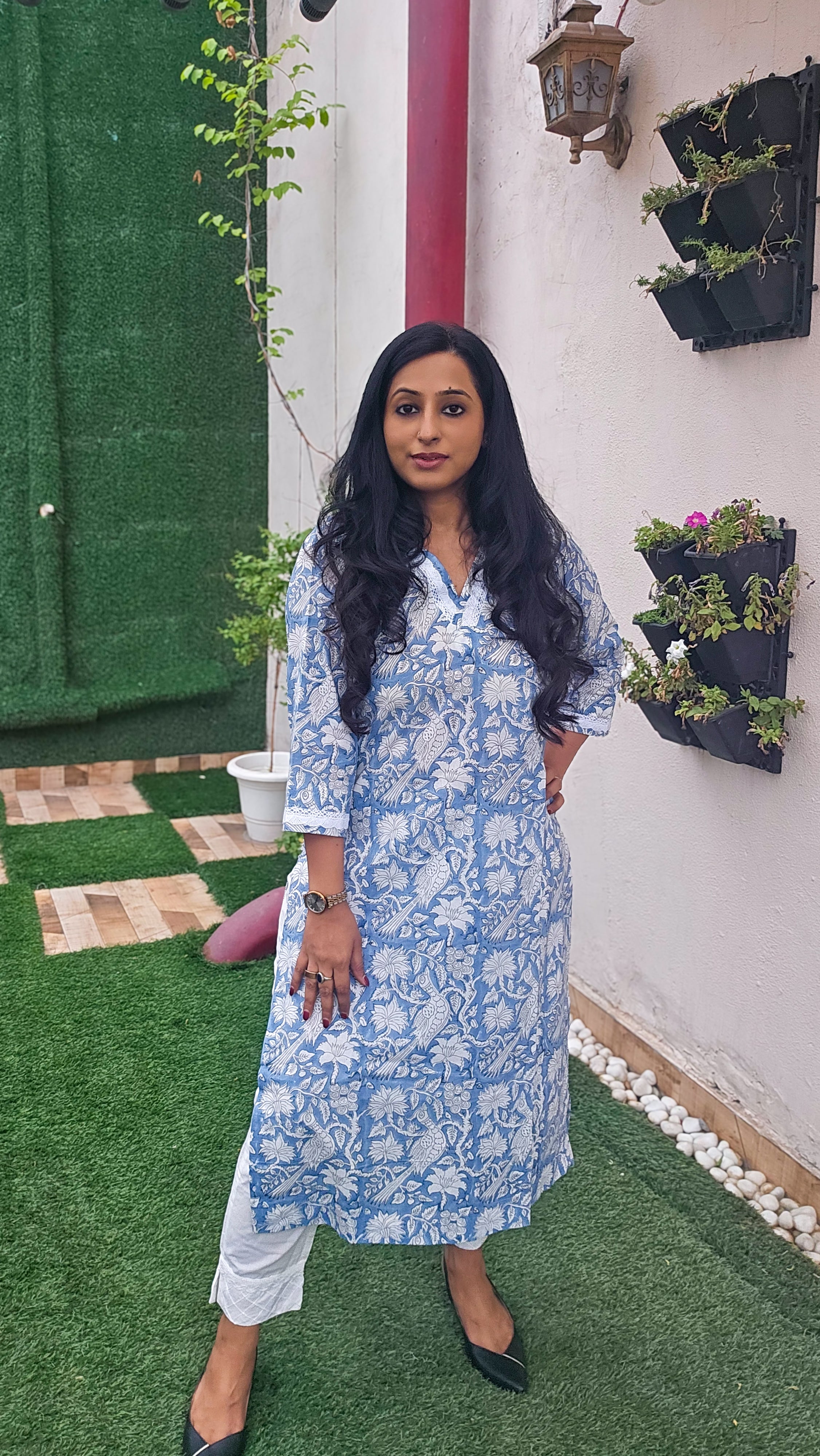 Woman wearing a blue floral with bird motifs hand block print kurta with white pants. Its a pure cotton kurta.