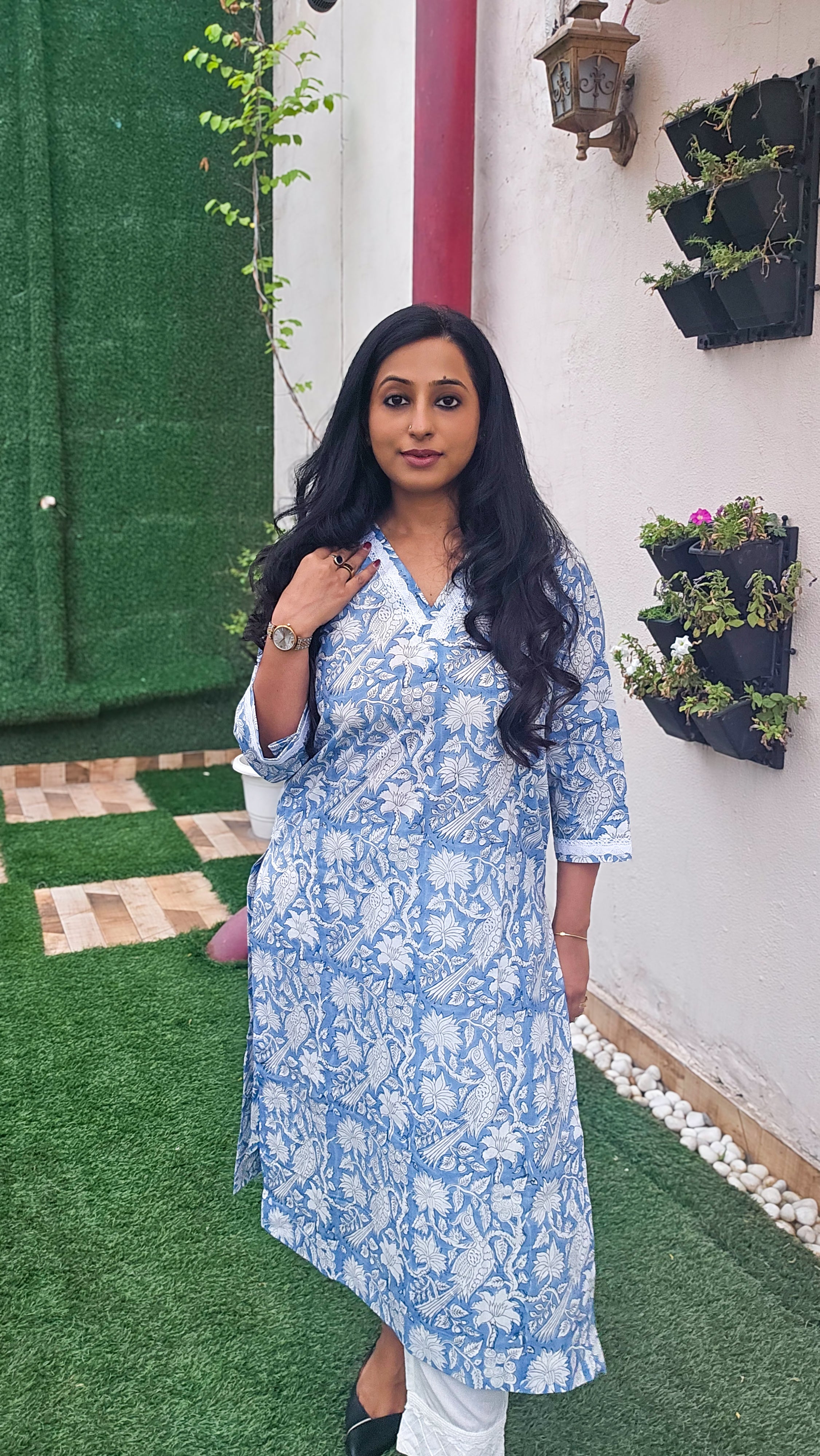 Woman wearing a blue floral with bird motifs hand block print kurta with white pants. Its a pure cotton kurta.