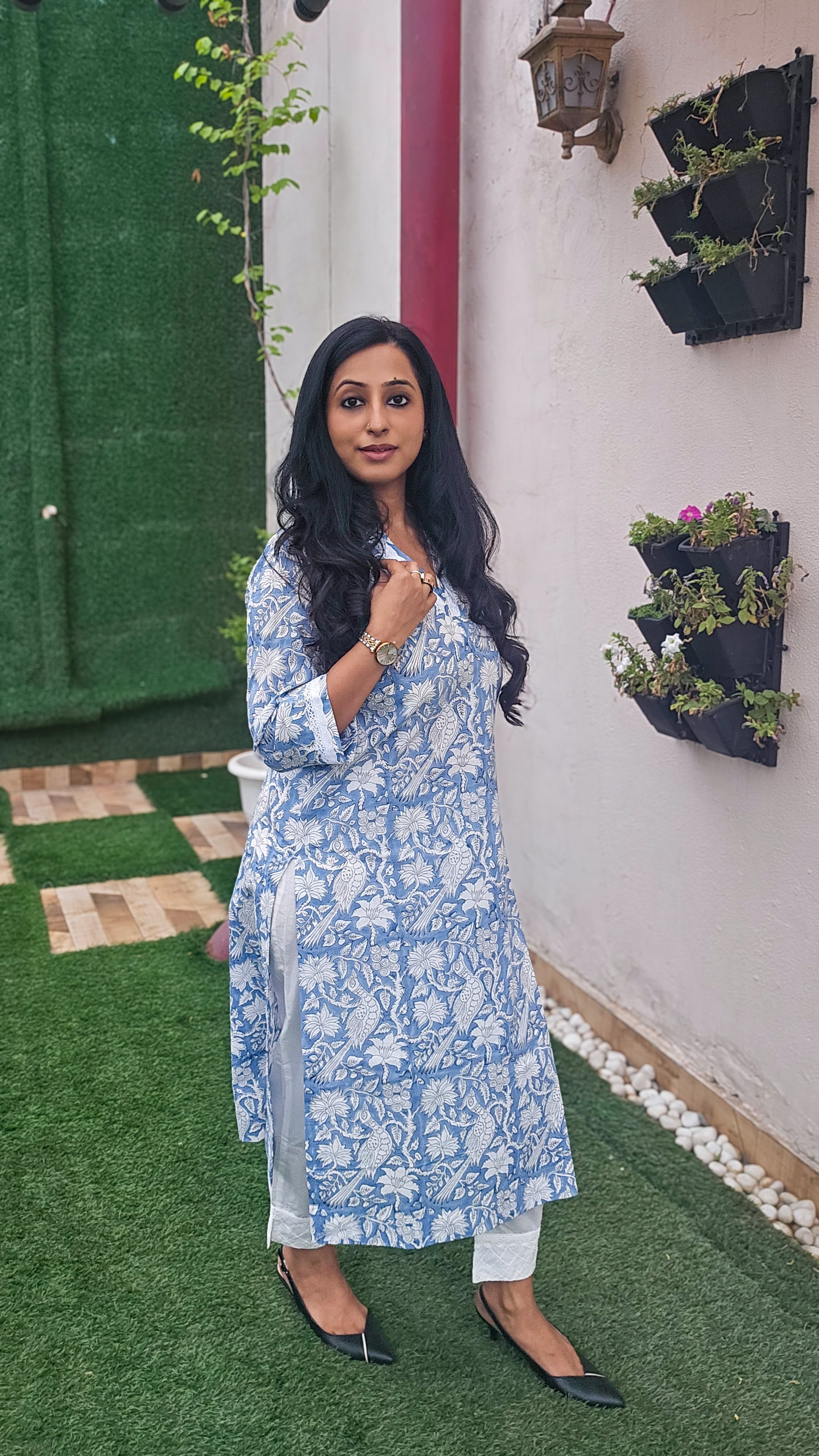 Woman wearing a blue floral with bird motifs hand block print kurta with white pants. Its a pure cotton kurta.