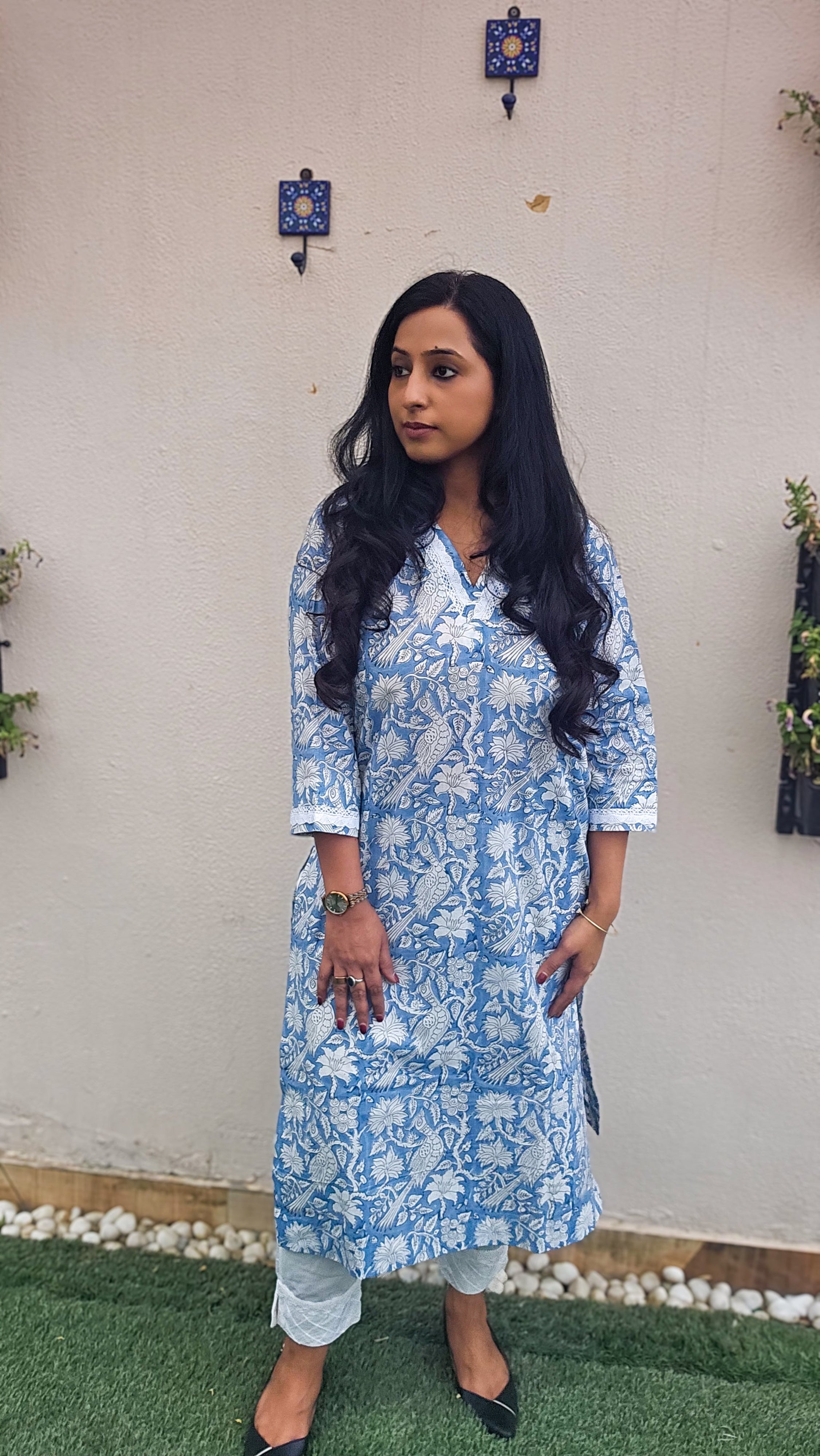 Woman wearing a blue floral with bird motifs hand block print kurta with white pants. Its a pure cotton kurta.