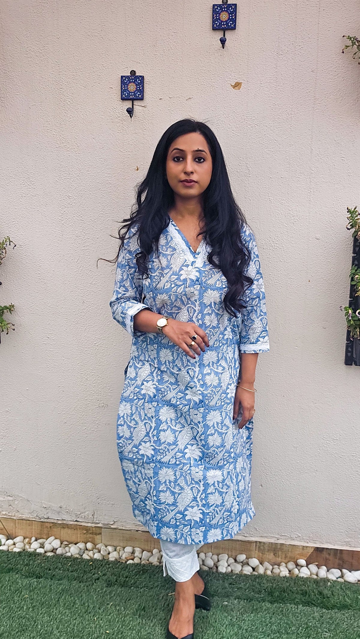 Woman wearing a blue floral with bird motifs hand block print kurta with white pants. Its a pure cotton kurta.