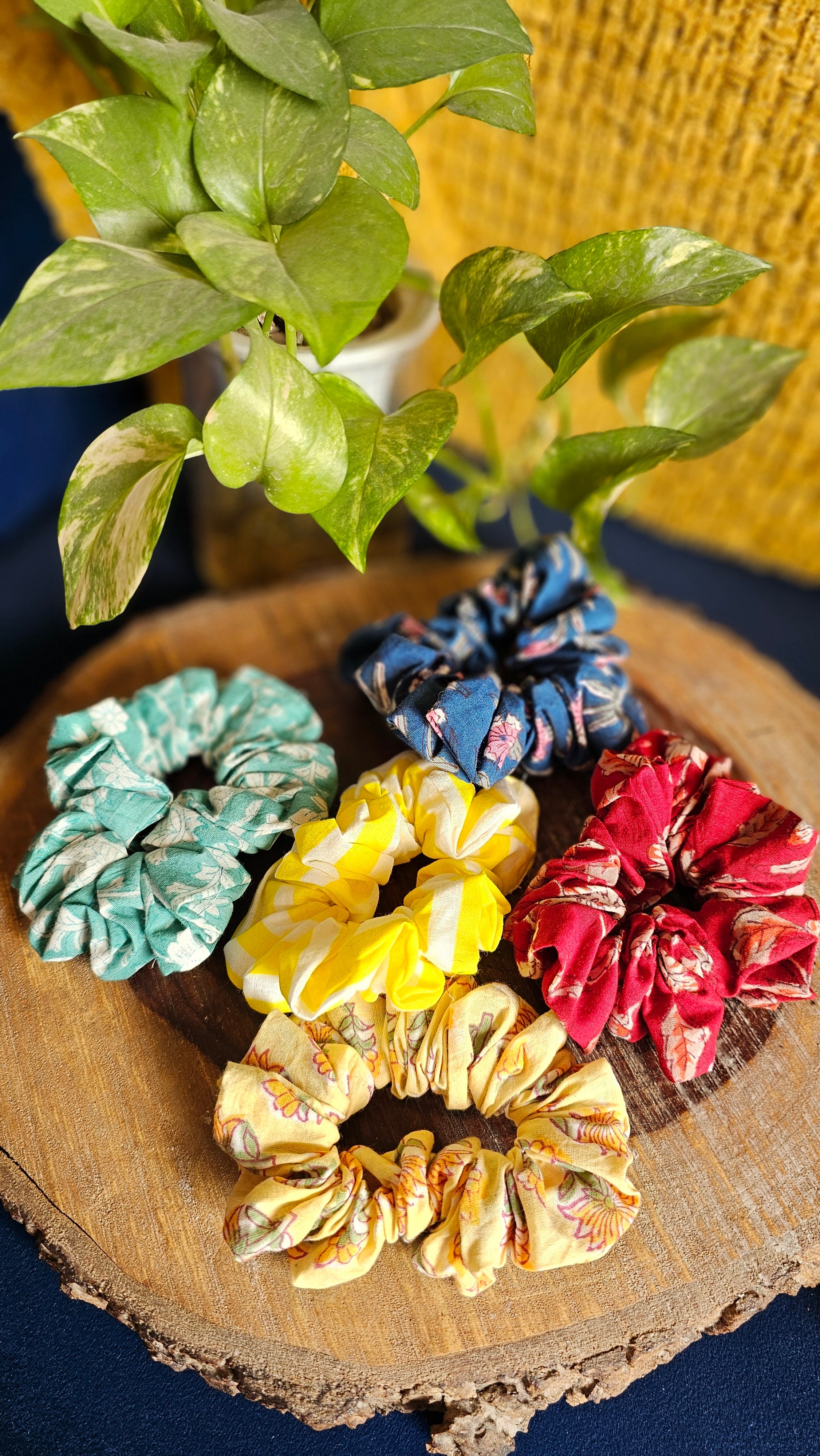 Colorful scrunchies on a wooden surface with a plant in the background
