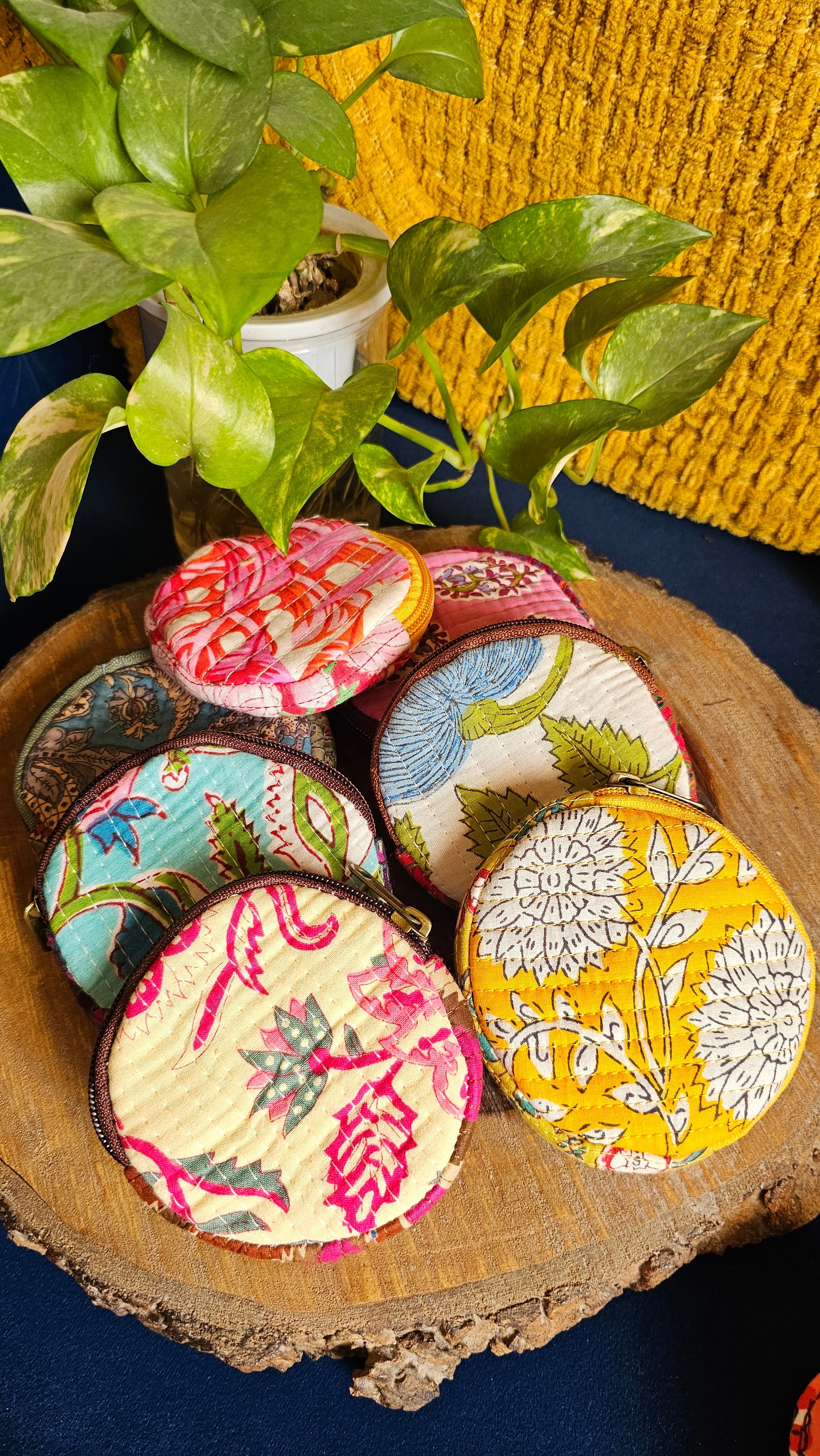 Colorful handblock print coin pouches on a wooden surface with green leaves.