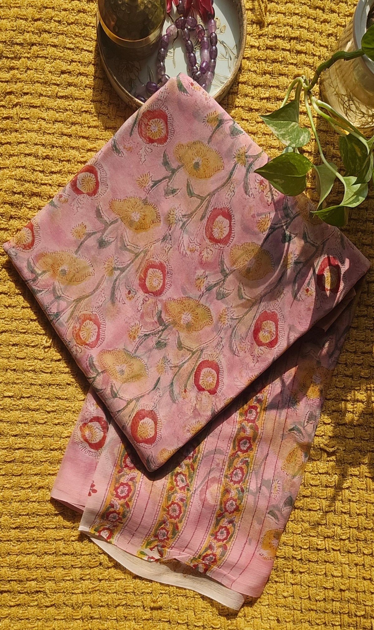 Floral-patterned fabric on a textured yellow surface with a glass and purple object in the background.