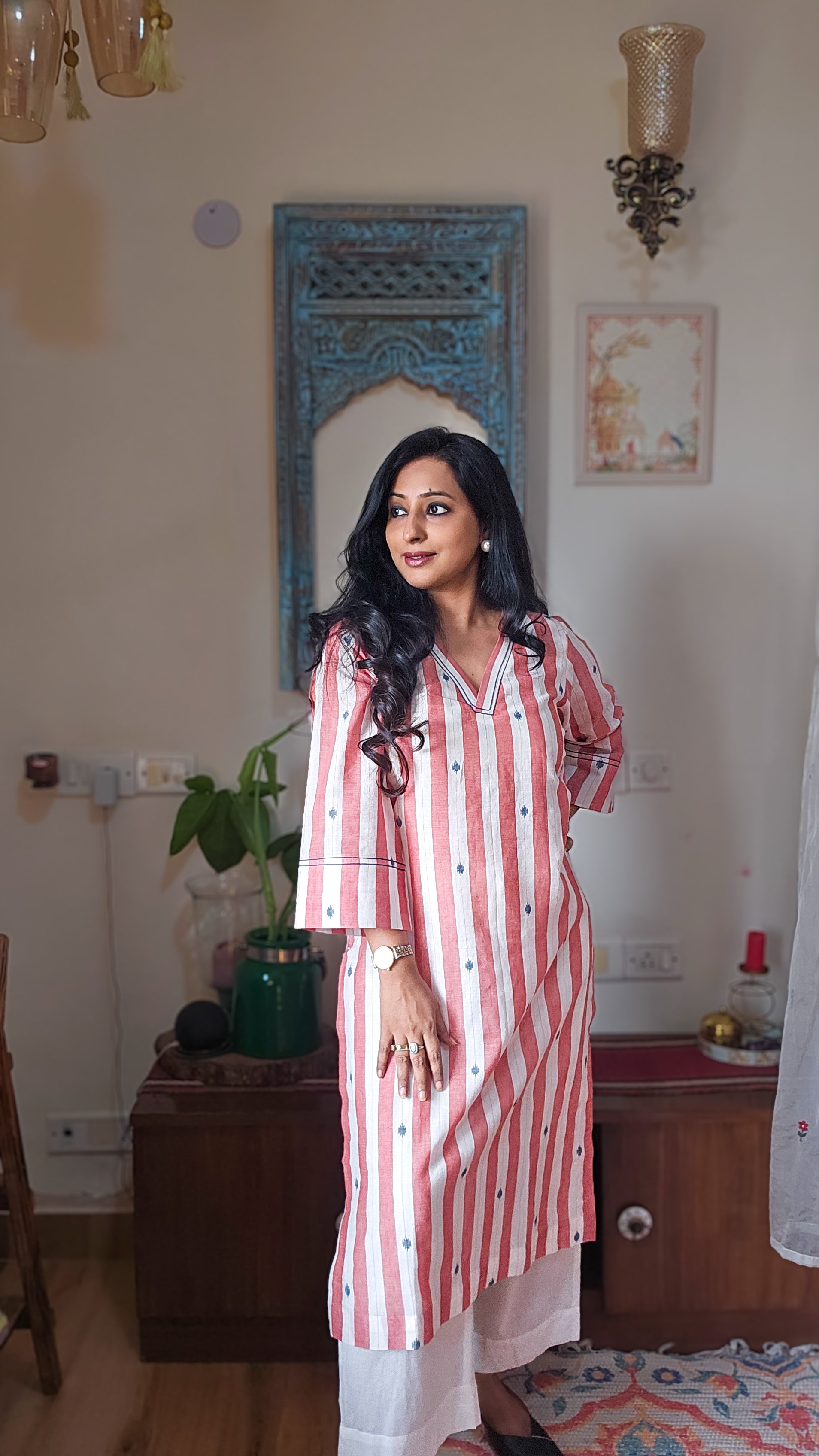 Woman in a red and white striped kurta standing in a room with decor elements.