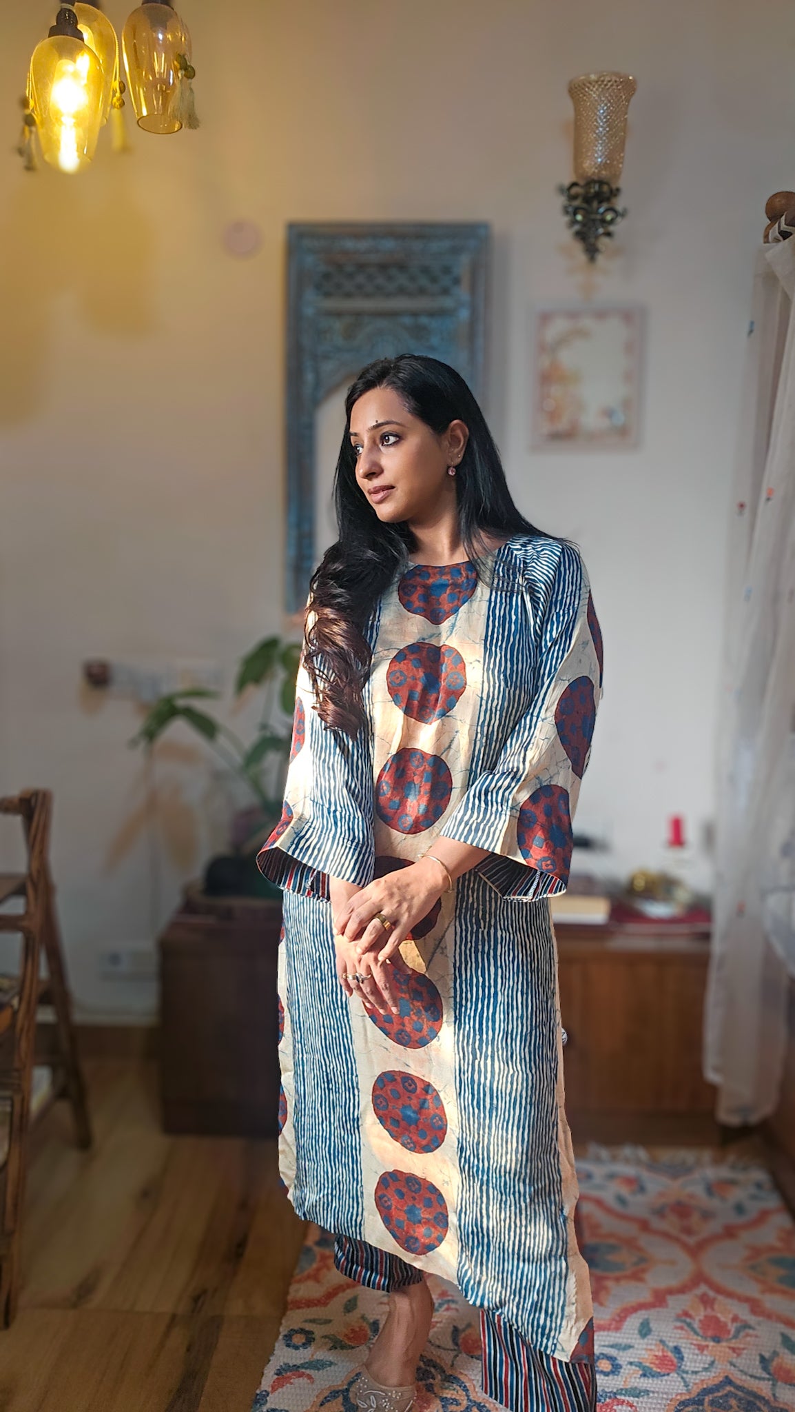 Woman wearing a patterned dress standing in a room with wooden floor and decorative elements.