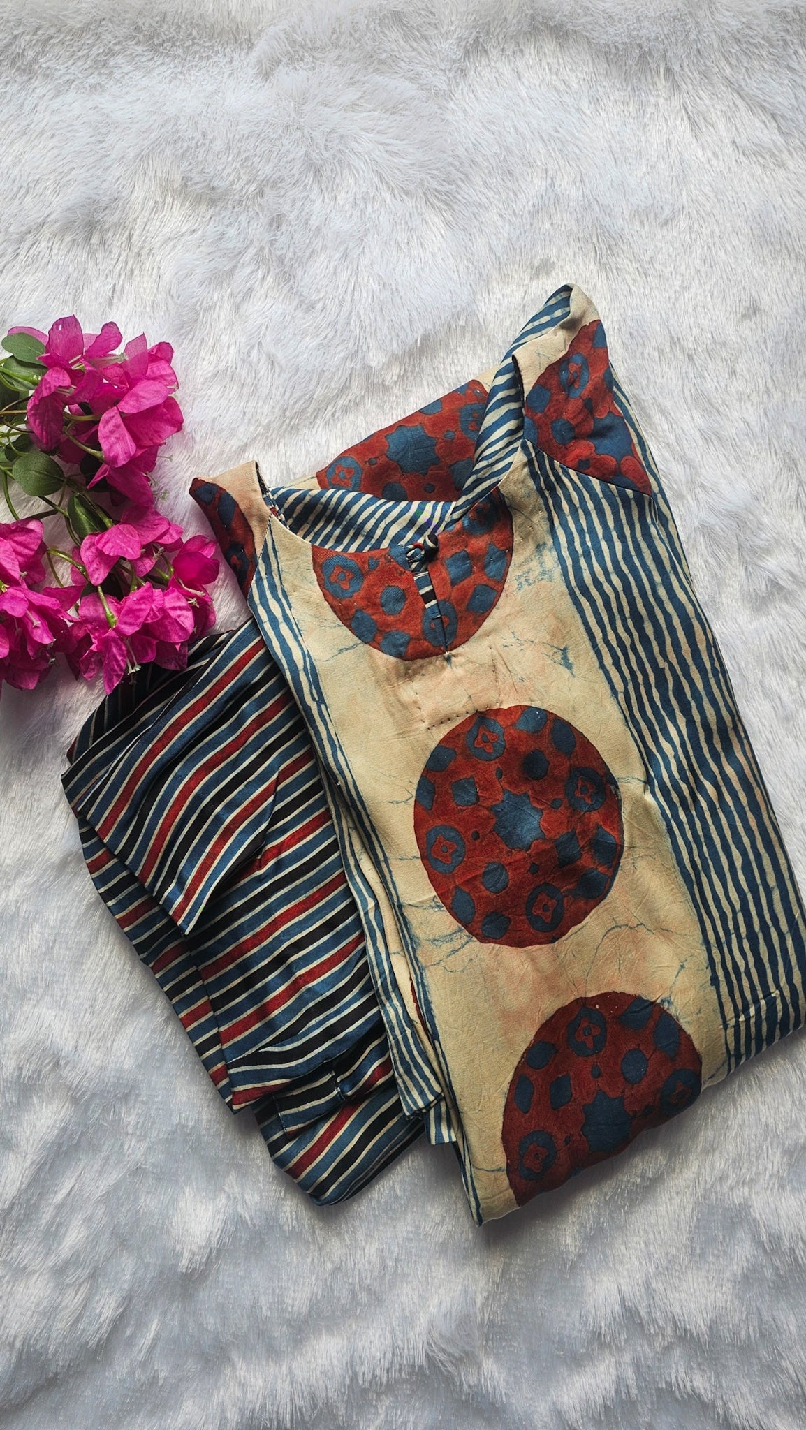 Textile piece with red and blue patterns on a textured surface with pink flowers.